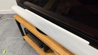 Sonos Arc Ultra soundbar on wooden bench below TV slight side angle