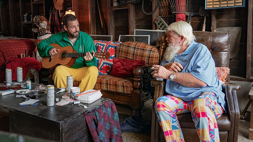 John Daly in polo and wild pants looking at Adam Sandler on a couch with his guitar in Happy Gilmore 2. 