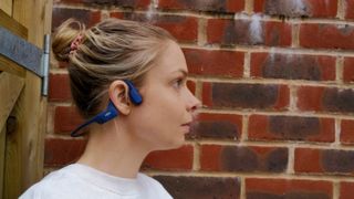 Shokz open run shown on a woman looking to the right with a brick wall behind