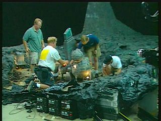 Technicians on a soundstage film a scene with miniature spacecraft on the floor of a miniature ocean.