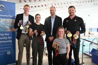 Prince William standing with Olympic swimmers Tom Dean, Adam Peaty, Maisie Summers-Newton and Louise Fiddes at a pool