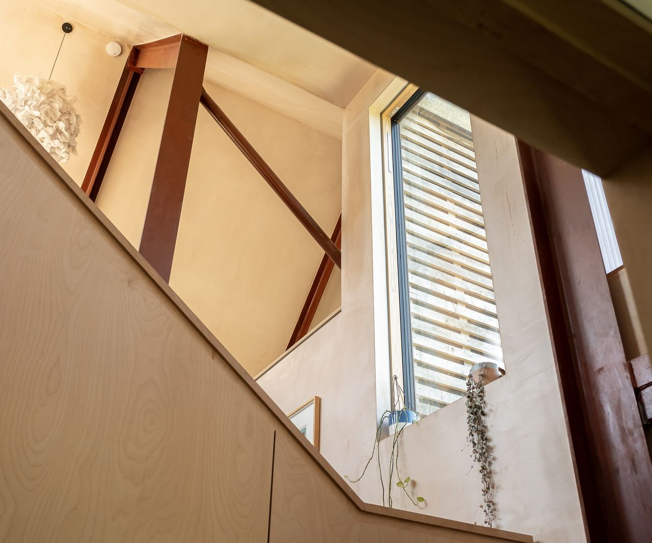 A close up angled shot up a timber staircase with a window bringing in natural light