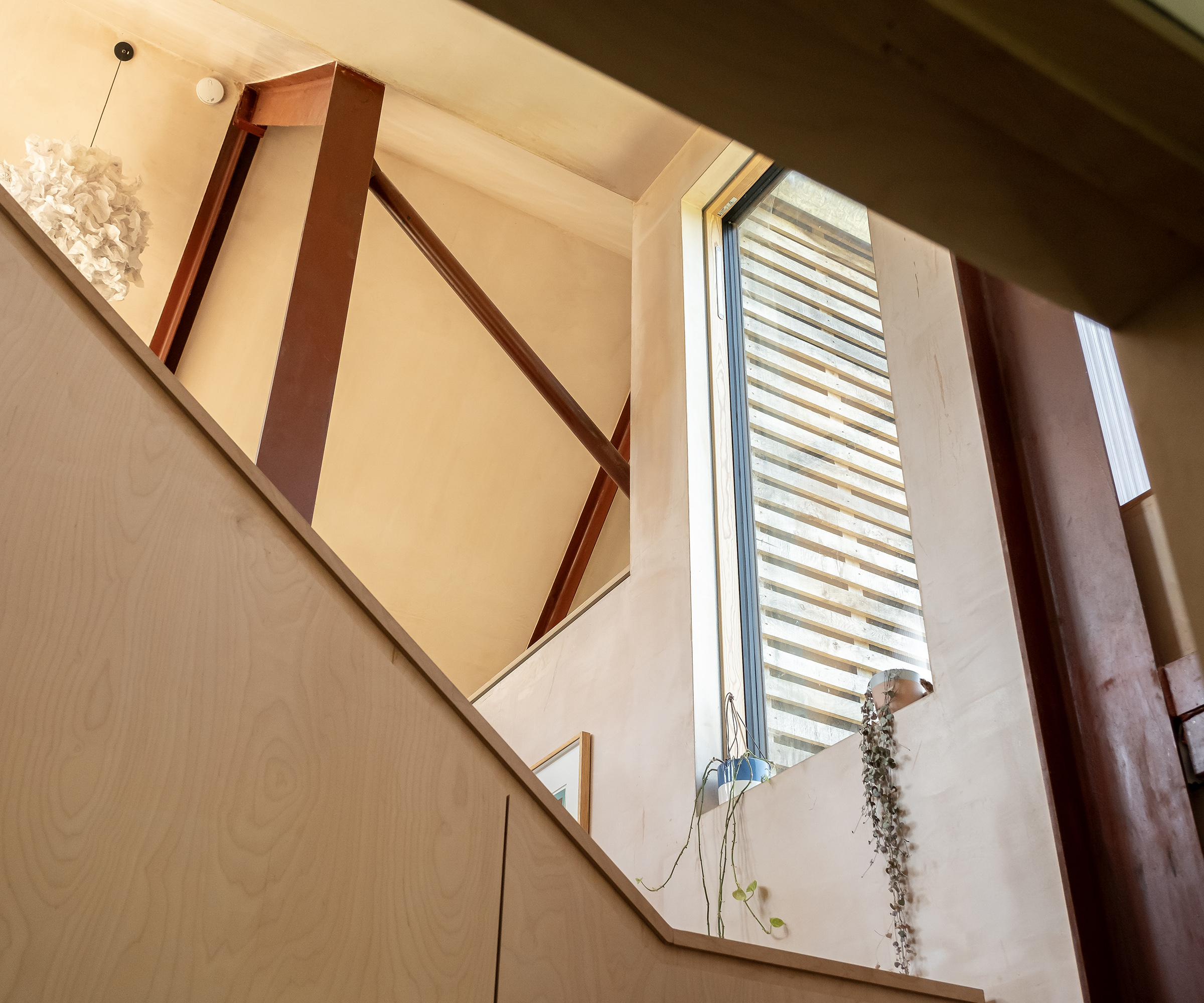 A close up angled shot up a timber staircase with a window bringing in natural light
