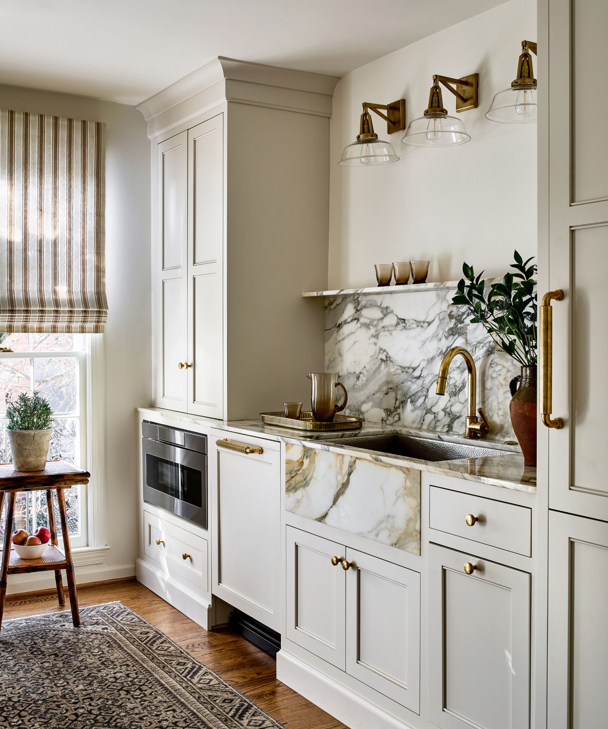 Neutral kitchen with painted cabinetry, marble sink and backsplash, wooden floor and persian rug