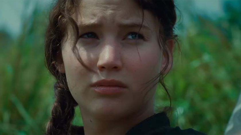 Jennifer Lawrence sitting in a field with her hair braided and looking concerned in The Hunger Games.