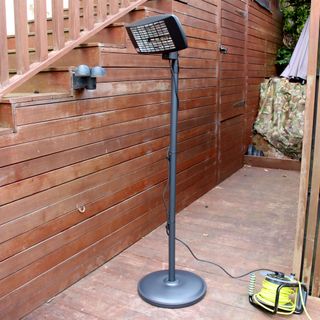 The Devola Core 2kW Freestanding Patio Heater plugged into a green and yellow outdoor extension lead on a wooden decked area