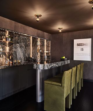 A dark, moody bar with green bar stools