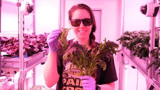 NASA scientist Jess Bunchek holding a freshly harvested bunch of rucola grown in the ISS EDEN greenhouse in Antarctica.