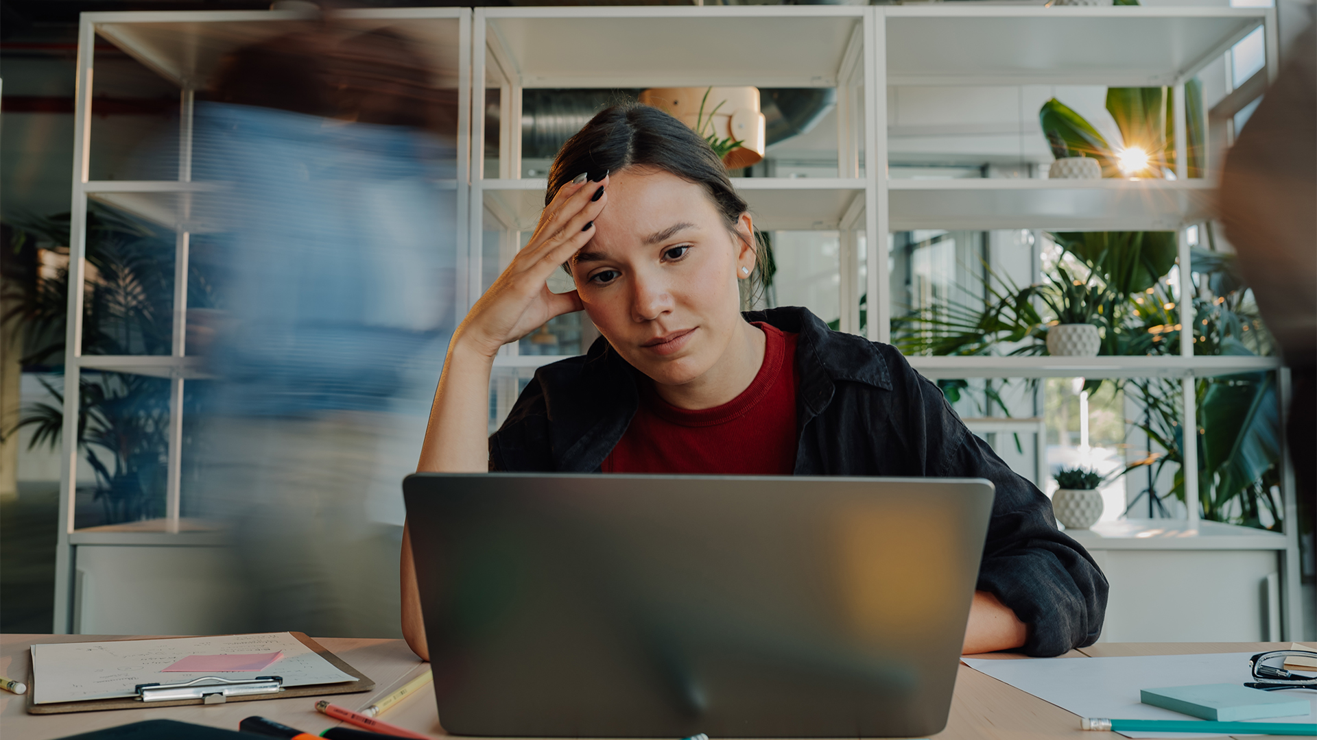 Female software developer working on laptop in open plan office space with frustrated, exasperated look on her face.