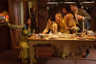 A group of people take a picture at an outdoor table as one woman stands off in the background, in 'Bad Sisters.'