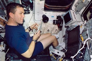 Astronaut Rick D. Husband wearing a blue t-shirt and blue shorts is working on the aft flight deck in the space shuttle Columbia.