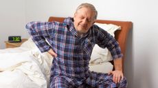Why do I have back pain? Man struggling to get out of bed and clutching his lower back