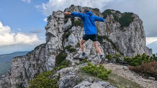 Ultra runner Galen Reynolds runs away from the camera along a mountain trail, both feet off the ground.