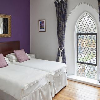 bedroom with white and purple wall and wooden floor and arched window and curtain