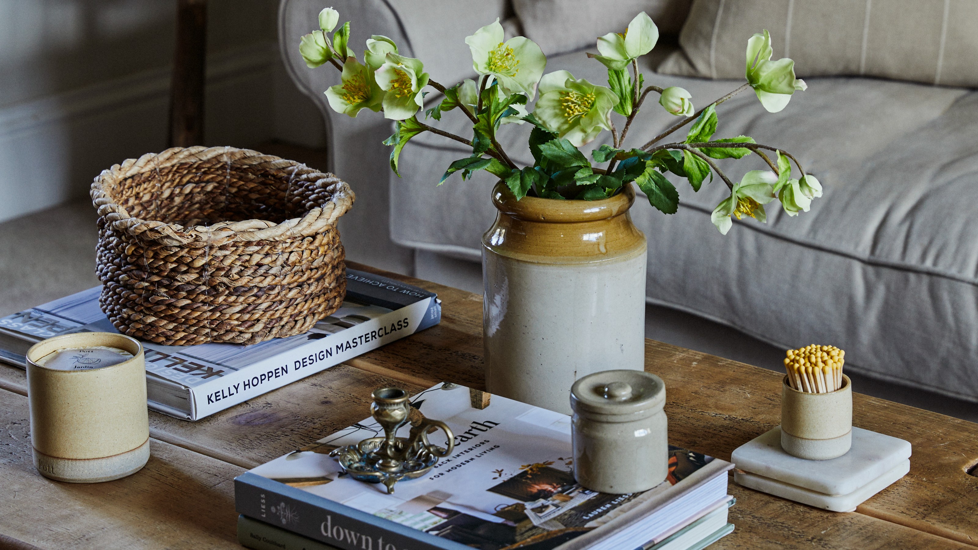 A living room with a rustic wooden coffee table styled with coffee table books, a vase of flowers and a scented candle from Pott with matching matchsticks