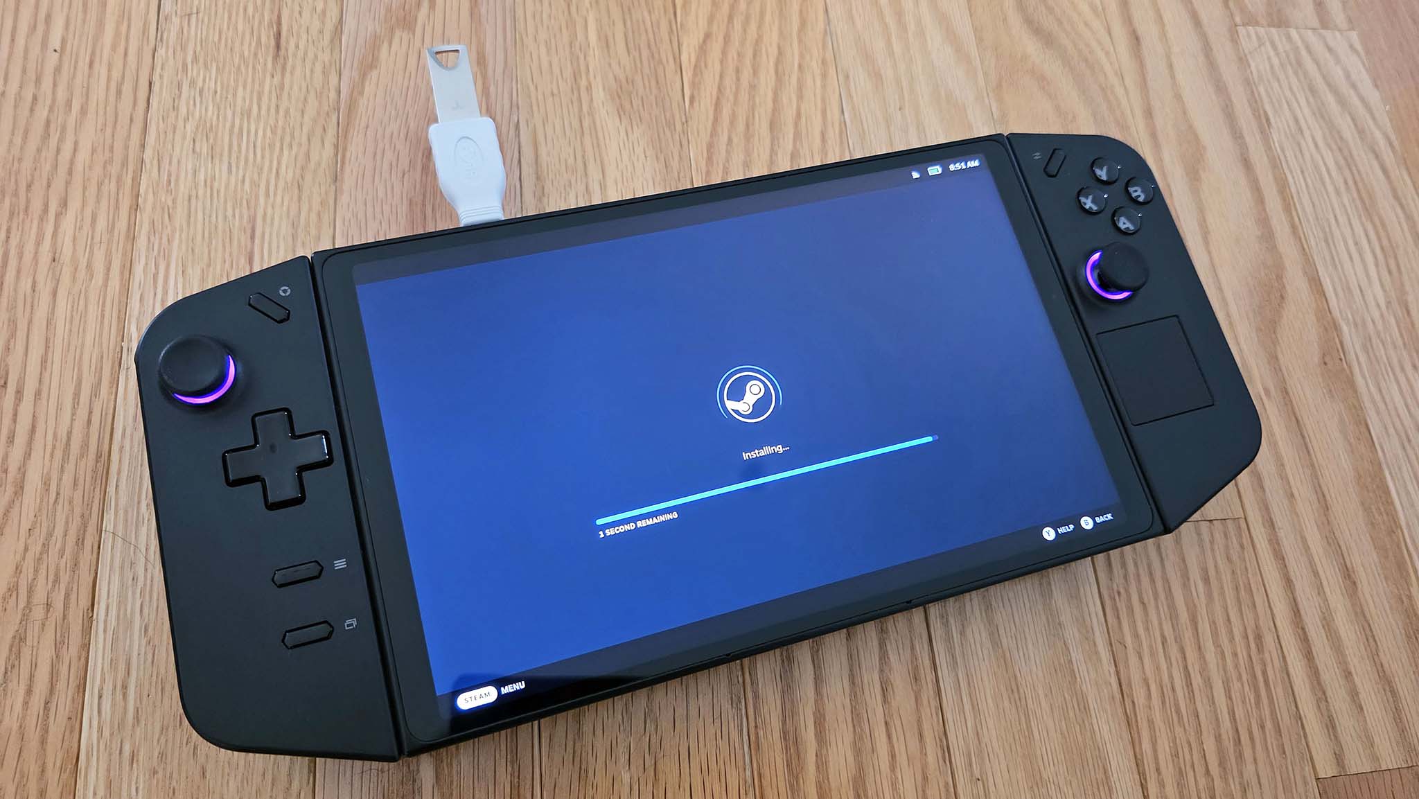 A Legion Go on a wooden desk with a USB stick in its top port and SteamOS installing on the screen.