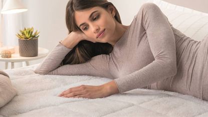 A woman lying on her side on top of the Dreamland Hunker Down Mattress Warmer