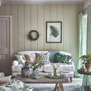 A living room with sage green wood wall panelling and a cream sofa with scatter cushions