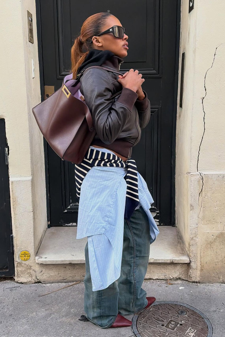 A woman wearing a brown jacket, blue jeans, and burgundy bag and shoes.