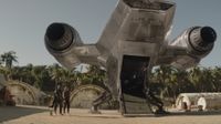 an armored sci-fi warrior in silver and a woman stood behind a spaceship.