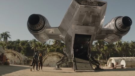 an armored sci-fi warrior in silver and a woman stood behind a spaceship.