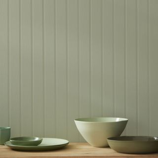 A light green paneled room with a wooden table and green bowls and plates