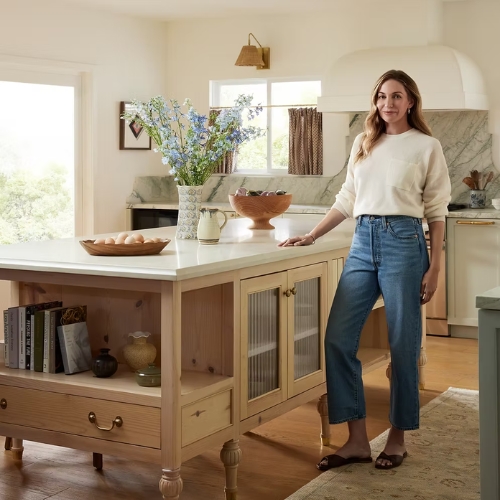 Image of a woman in jeans and a cream sweater standing in a traditional kitchen.