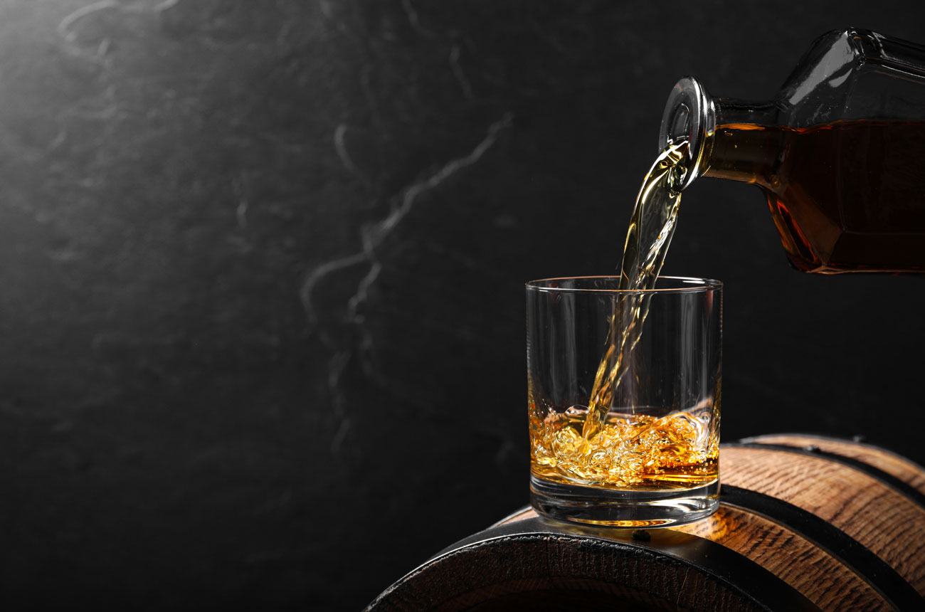Pouring whisky into a glass on top of a barrel