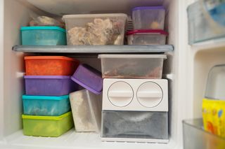 Multicoloured plastic food storage containers stacked in a freezer