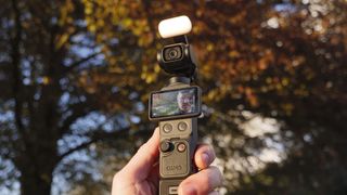 DJI Osmo Pocket 4 vlogging camera with natural background at golden hour, and the user in the frame of the screen