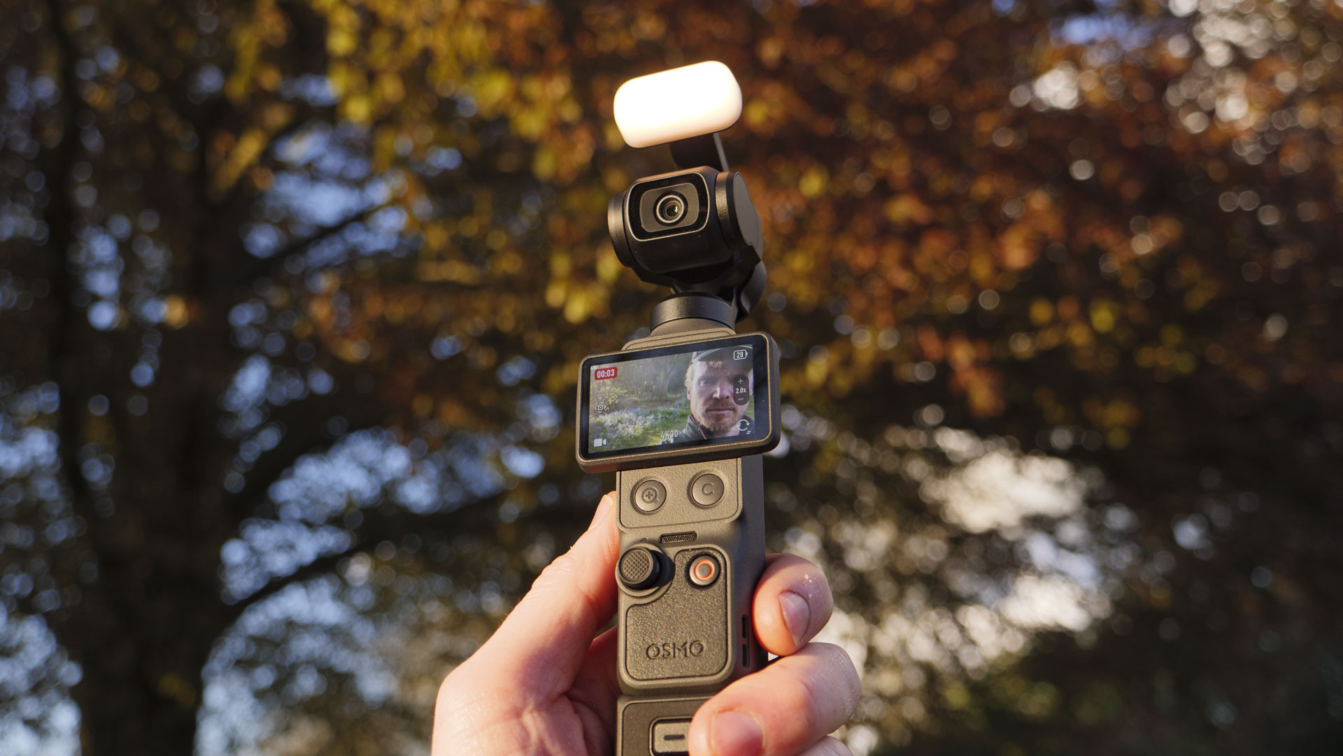 DJI Osmo Pocket 4 vlogging camera with natural background at golden hour, and the user in the frame of the screen