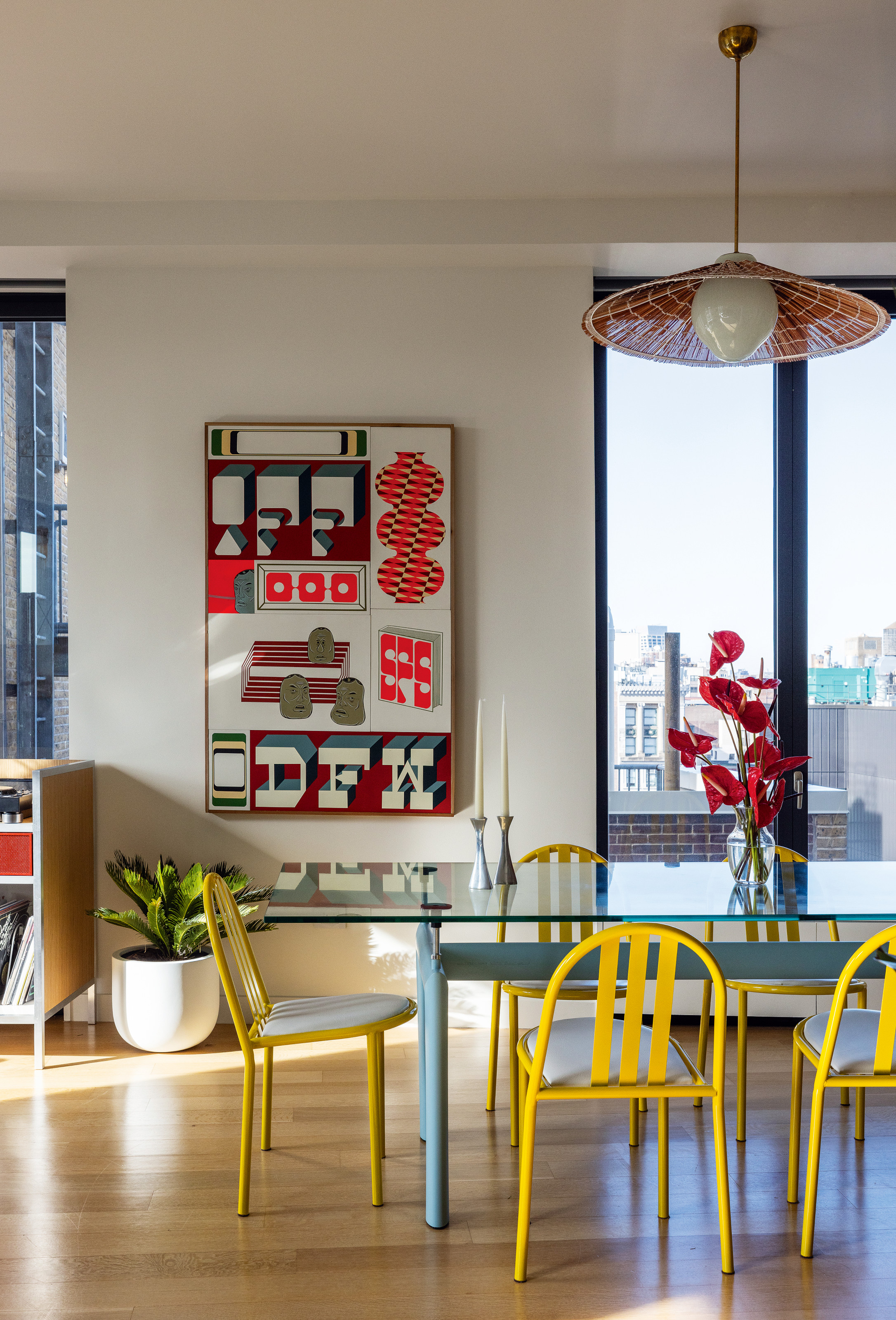Dining room with white walls, red, white and blue typographic print, red pendant, blue table and yellow dining chairs