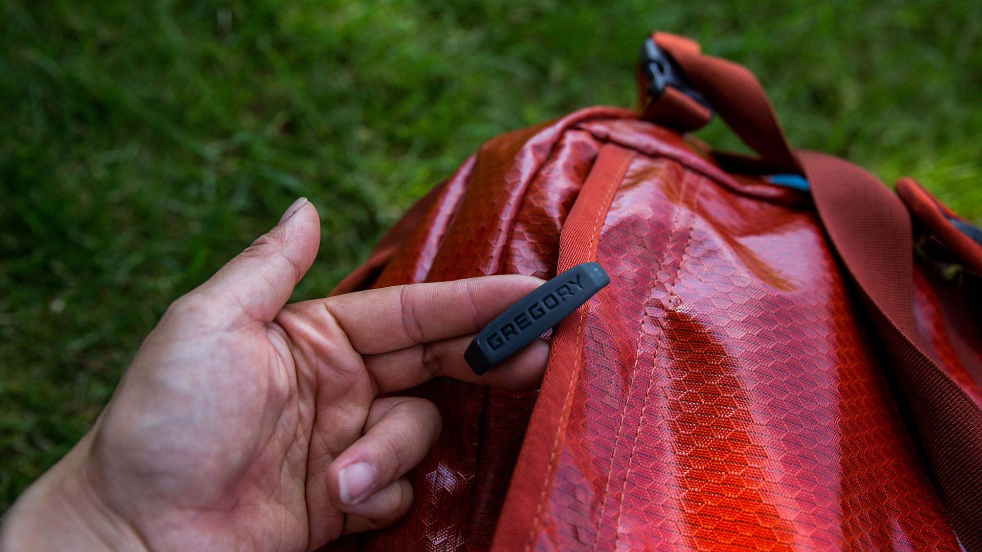 A close-up of a Gregory Alpaca 60 duffel bag, with a hand holding up the branded T-grip zipper.