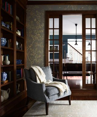 dark home office study with dark wood floors, french doors and walls lined with mahogany book shelves with a comfy armchair