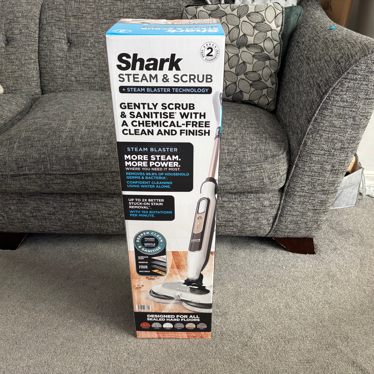 Shark Steam &amp; Scrub branded packaging positioned on grey carpet in front of grey sofa
