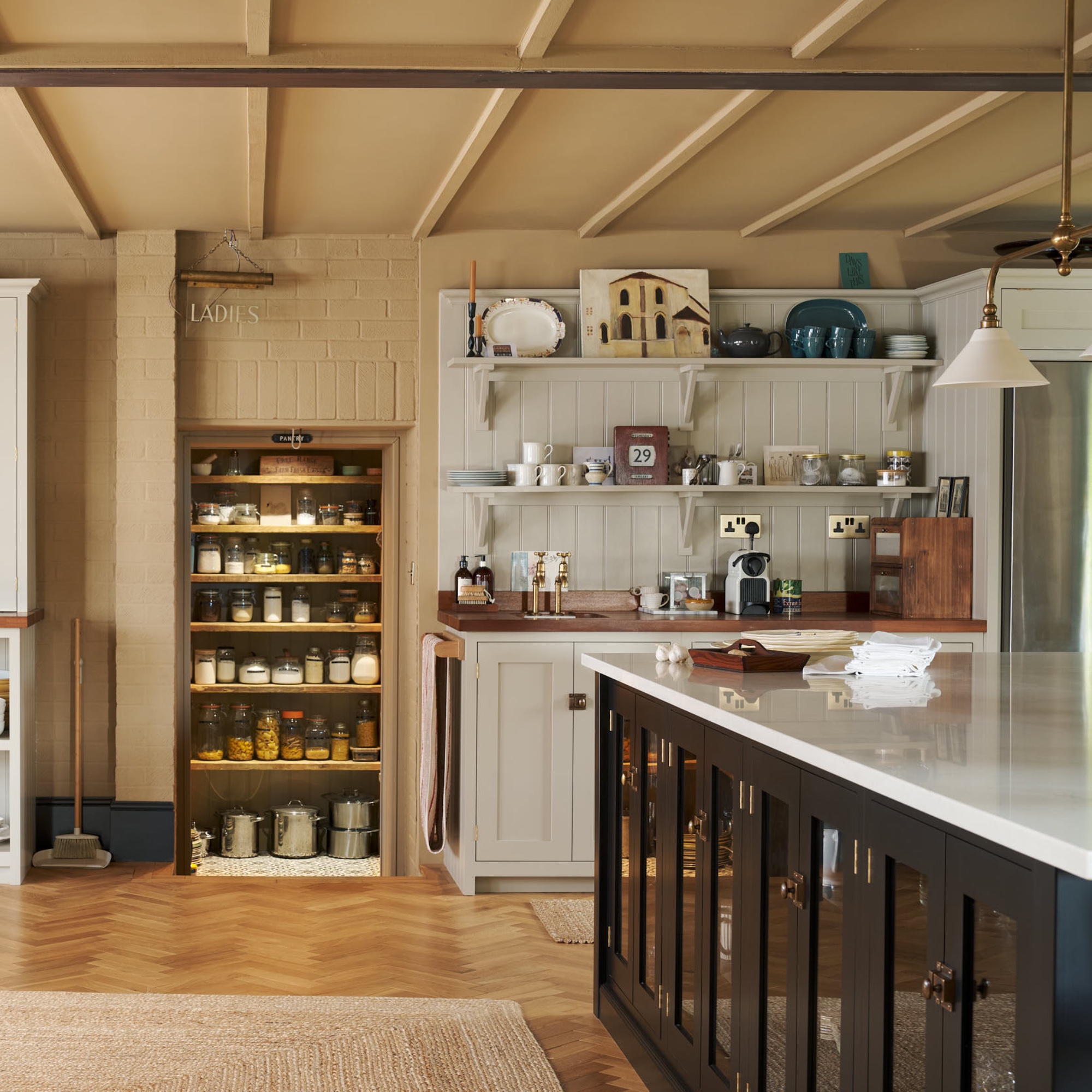 walk in pantry with lighting, black kitchen island with storage and white worktop, parquet flooring and rug, tea and coffee station