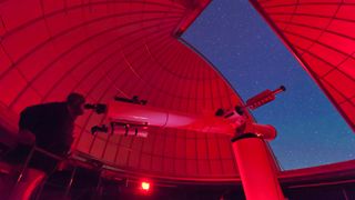 Inside the observatory, an astronomer makes observations with a large refractor telescope at the 3RF astronomy campus in Texas.