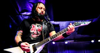 Monte Pittman of Ministry plays a riff on his white ESP V against a black and purple background.