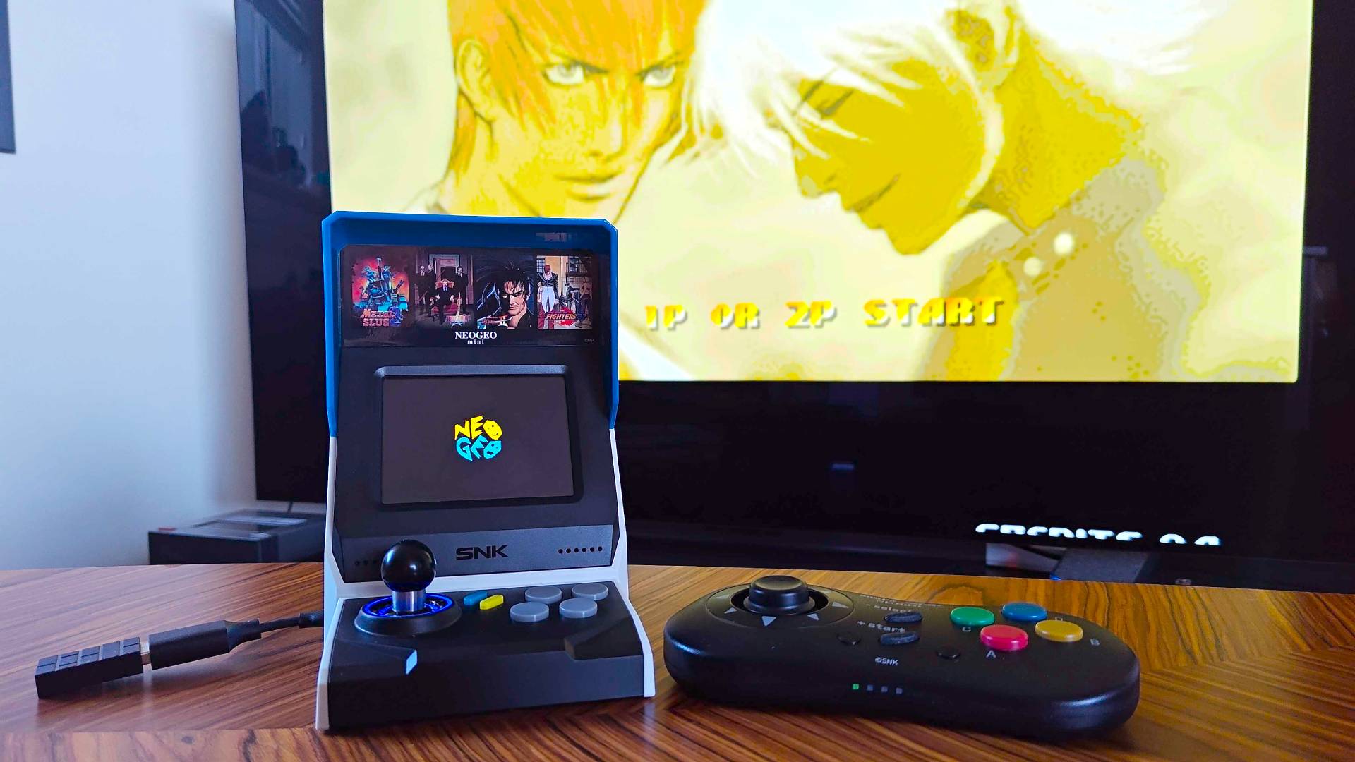 Neo Geo Mini next to 8Bitdo controller on woodgrain table.