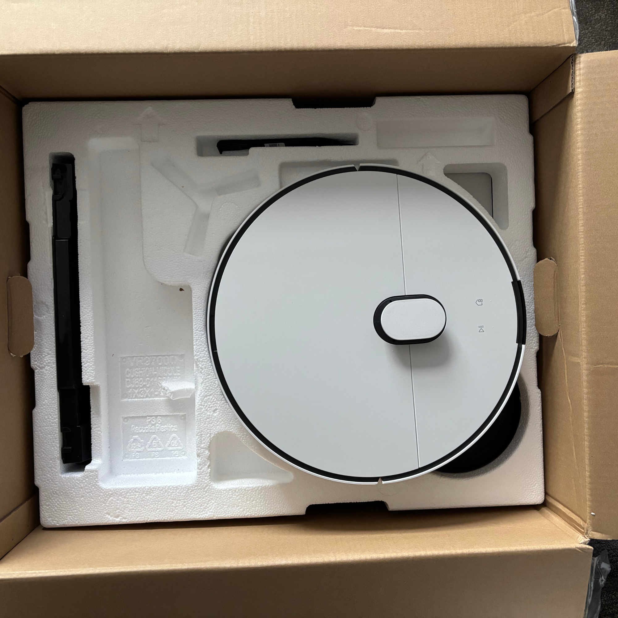 Opened cardboard box view featuring robot vacuum cleaner sitting on a layer of polystyrene packaging 