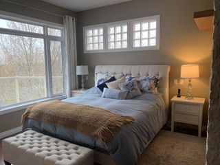 A small bedroom with gray walls, a stuffed headboard and matching ottoman, and a ochre throw on the bed