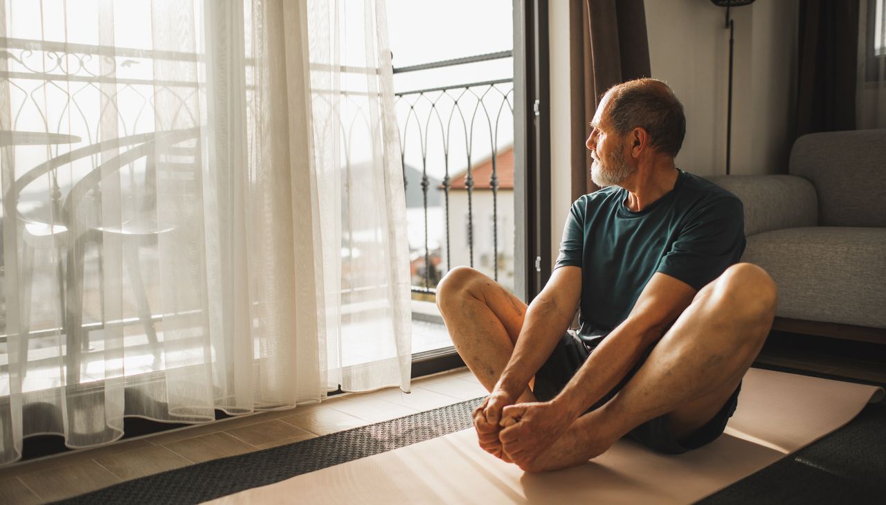 Man sitting on floor in butterfly stretch, looking out of window