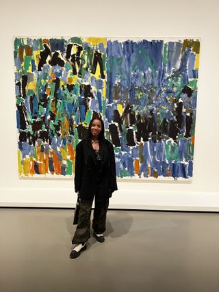 Lindsay Adams in a black blazer and green pants standing in front of a colorful painting.