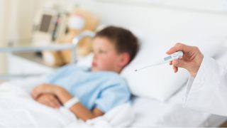 child in hospital bed next to doctor with thermometer