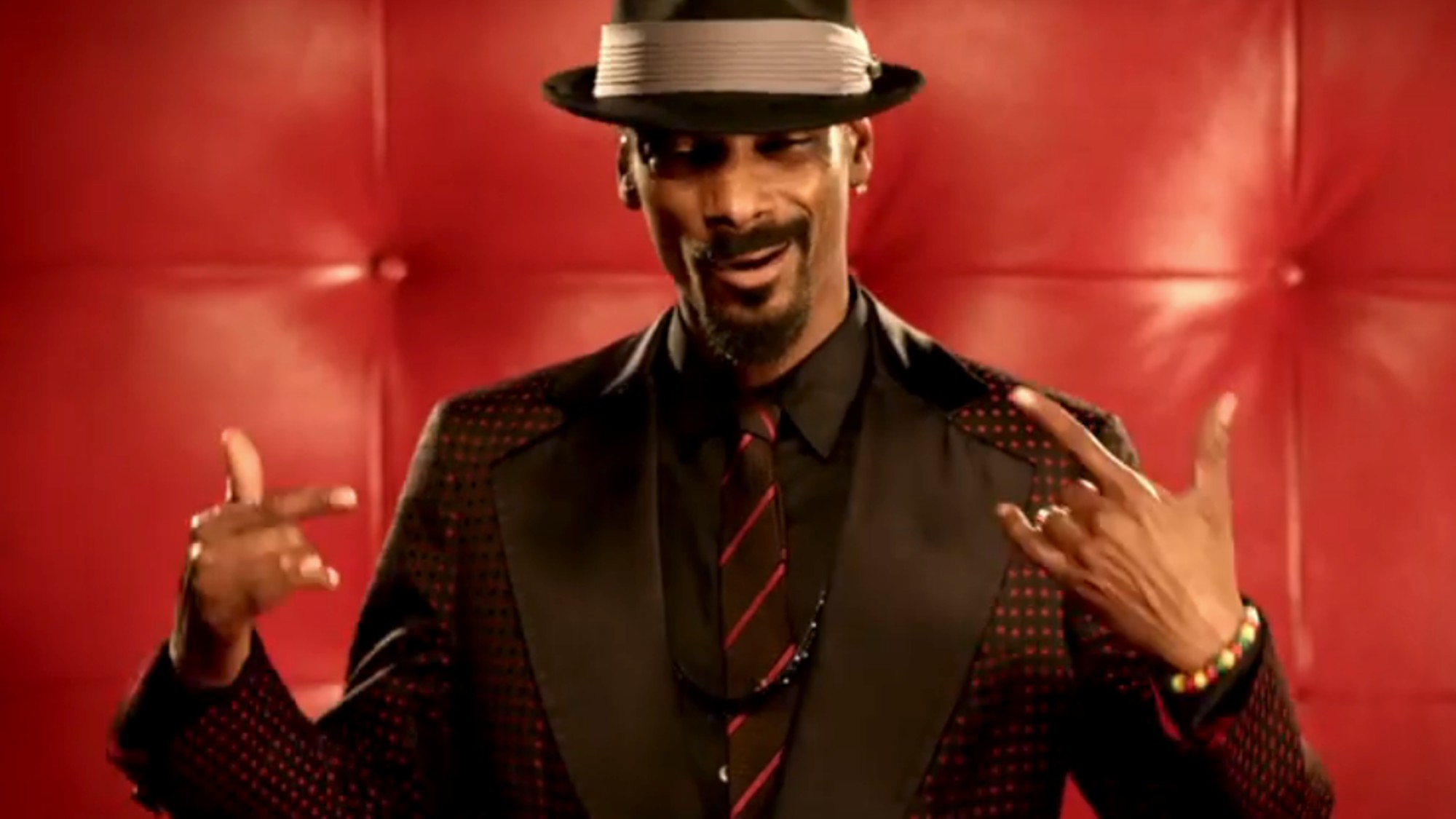 Snoop Dogg in a black and red suit, wearing a fedora.