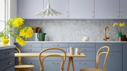 A qhite kitchen with light blue kitchen cabinets and a ywllow kitchen table and chairs. large yellow flowers, and a fluted milk glass light pendant above