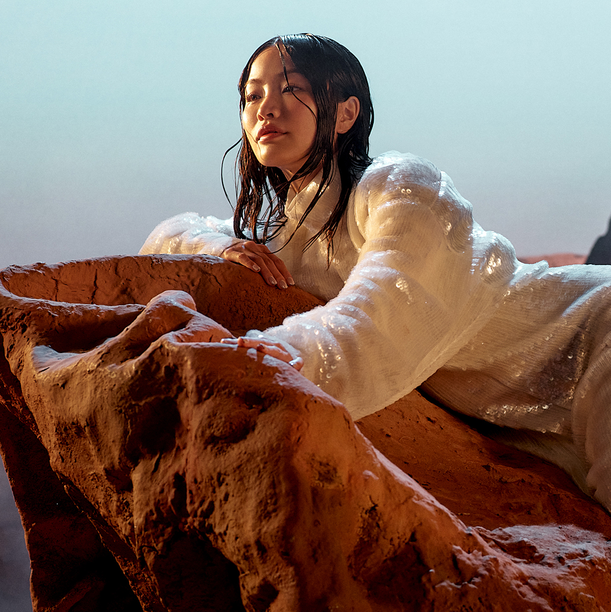 Anna Sawai reclines on red desert rocks in a dark textured top and a shimmering skirt.