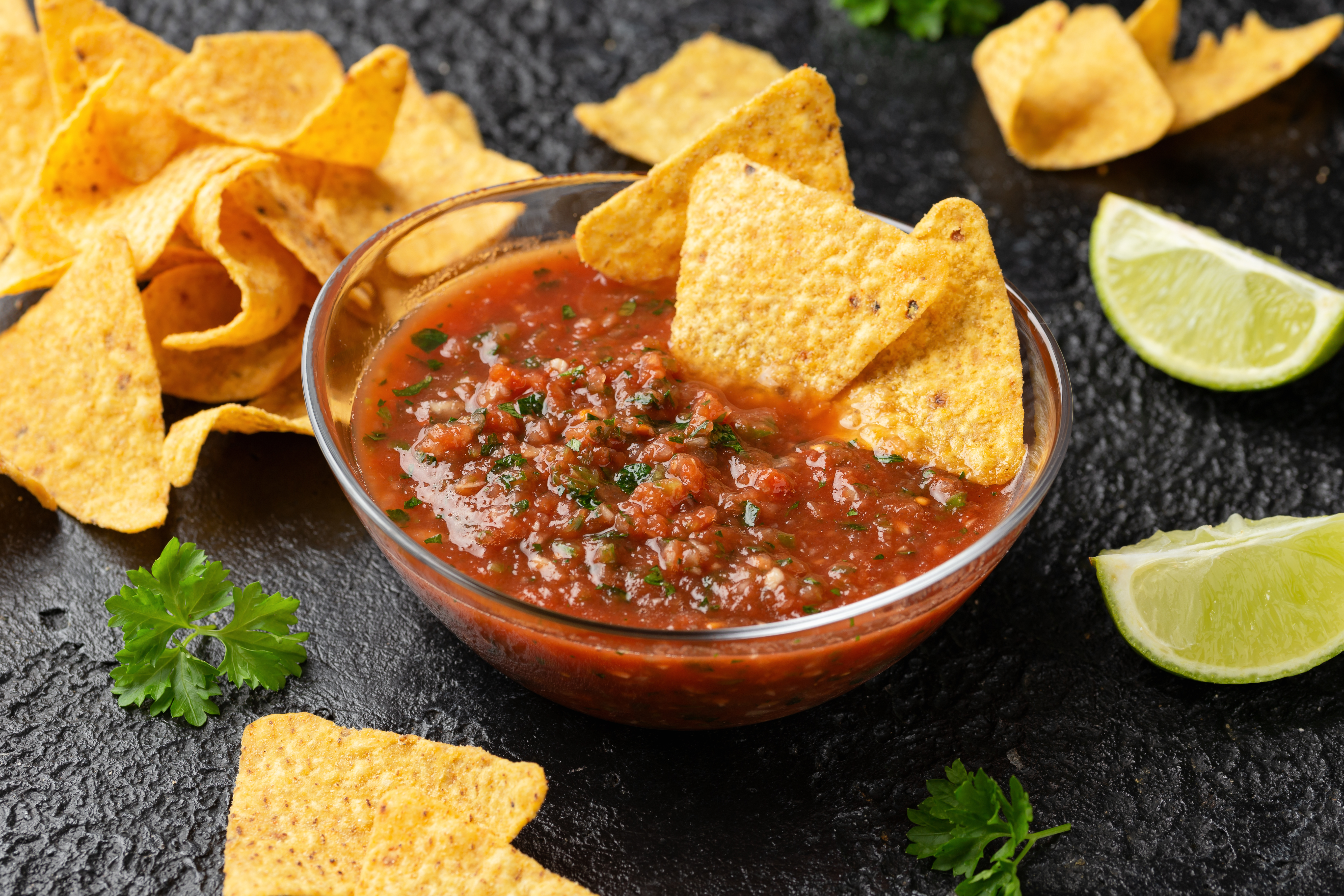 A bowl of red salsa with tortilla chips around it