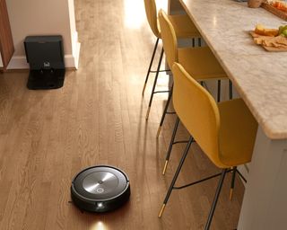 iRobot J7+ in kitchen with yellow bar stools on laminate wooden flooring