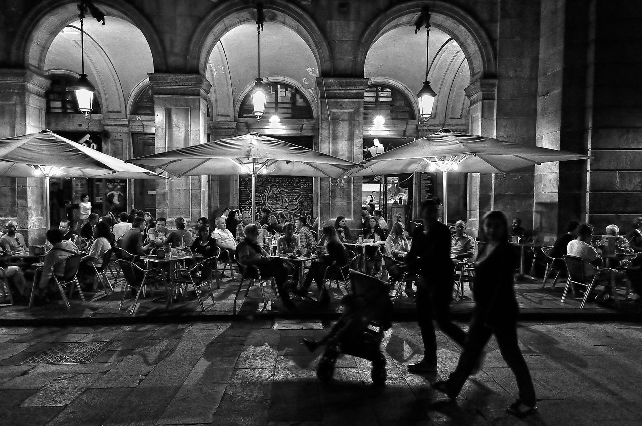 Black and white image of people dining under street light, captured on the streets of Barcelona